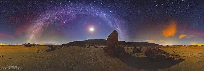 Starry night from the Teide National Park (Tenerife, Spain). We can see Mount Teide, near the centre of the picture, and the Moon within the arch of the Milky Way, behind a volcanic landscape with large rocks in the region of “The San José Mines”. An unco