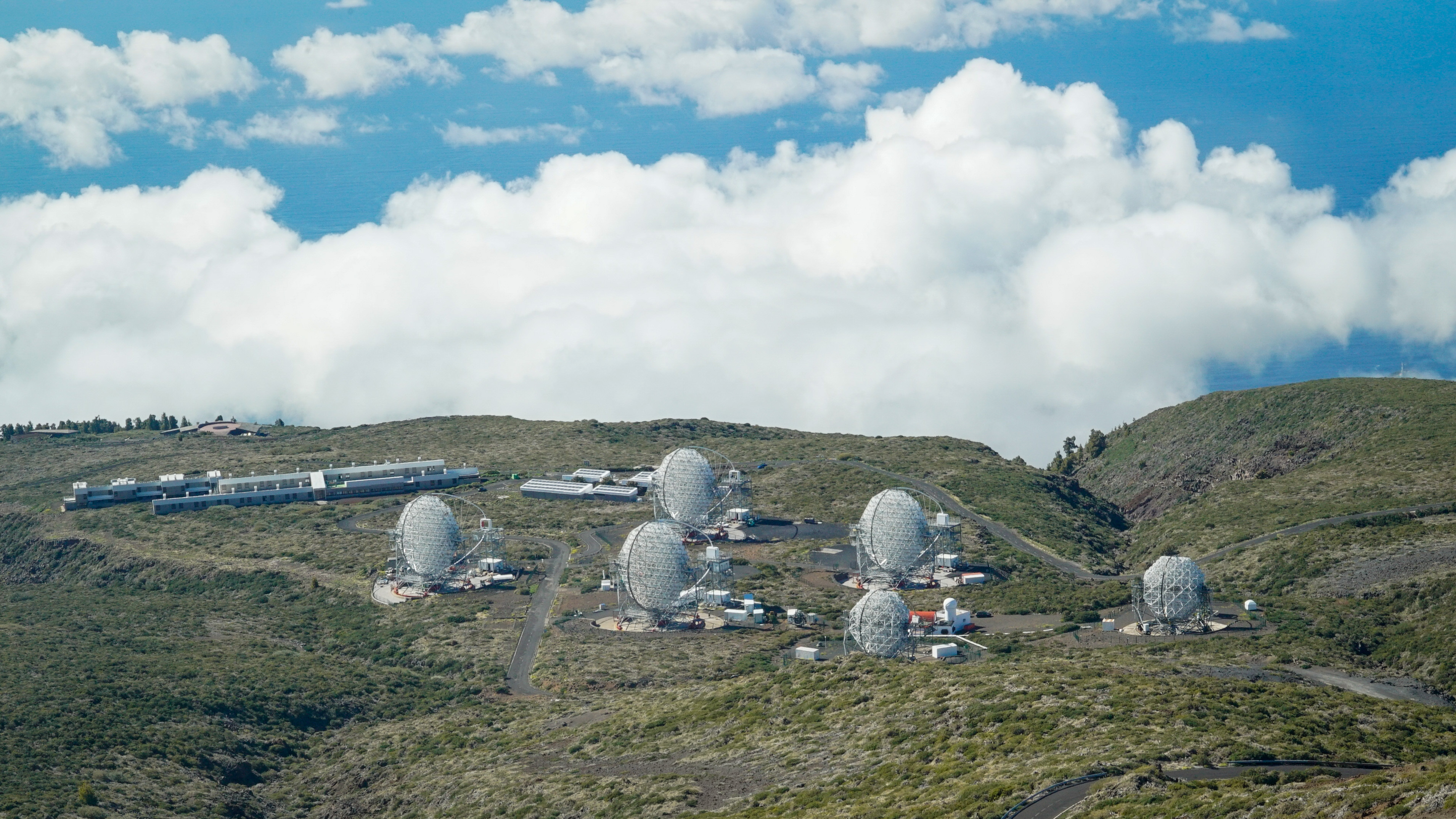 View of the four LSTs at CTAO-Norte and the MAGIC telescopes from the summit of Roque de los Muchachos. On the left, the ORM residence next to the Visitor Centre (in the background).