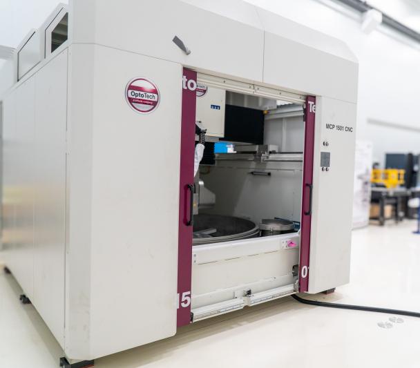 A large white machine with two big doors (polishing machine for large surfaces) in a white room with high ceilings (IACTEC's south clean room).