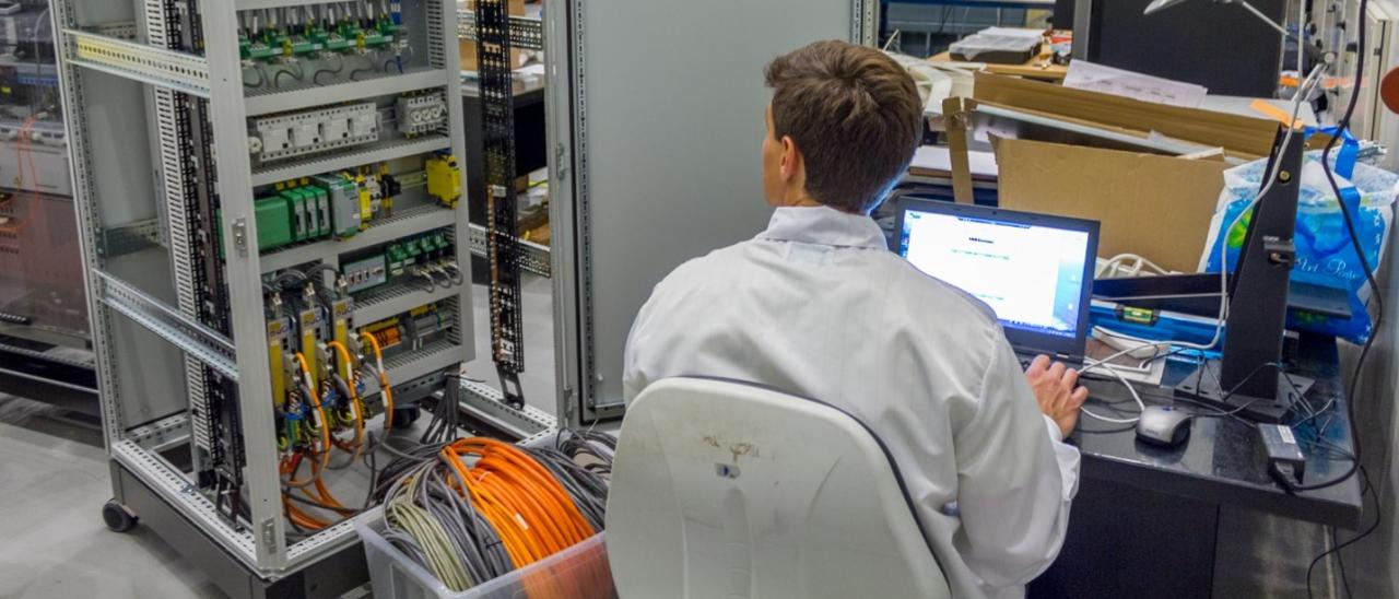 Imagen de un ingeniero trabajando en la electrónica del sistema de óptica adaptativa para GTC en el laboratorio. Ingeniero sentado trabajando en un ordenador con un armario de electrónica abierto a su lado