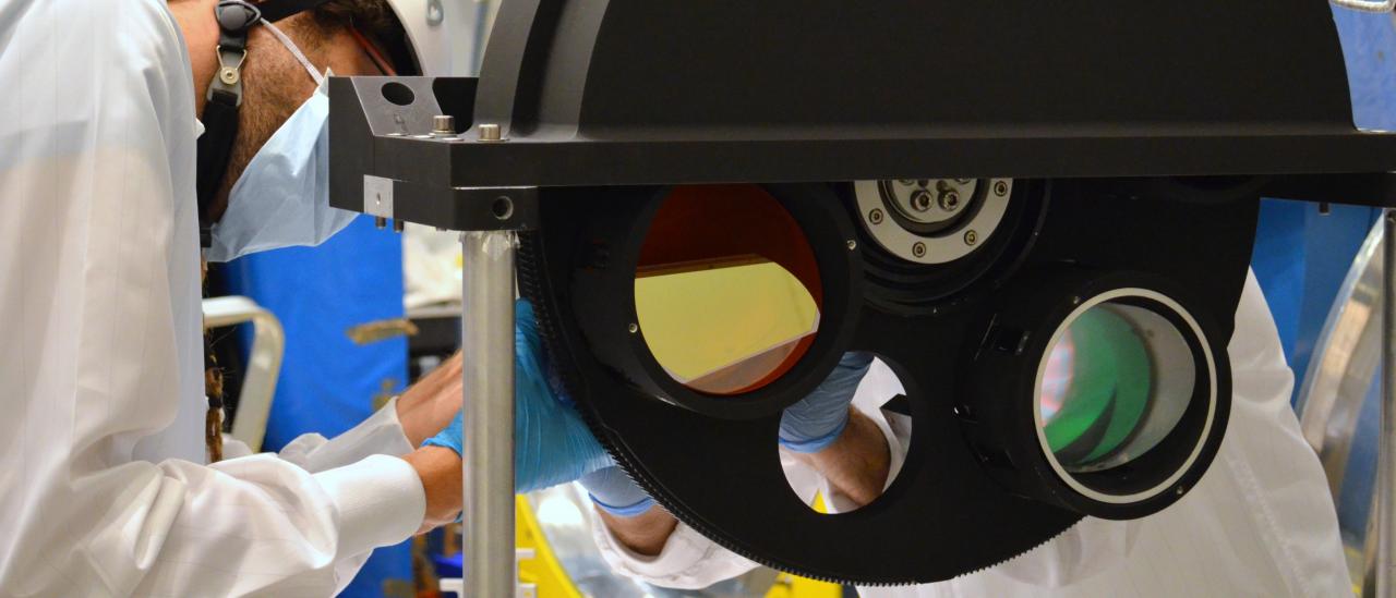 Image of an engineer working on the final assembly of the grisms wheel of the EMIR instrument in the laboratory. Large black metal wheel with holes for optical components