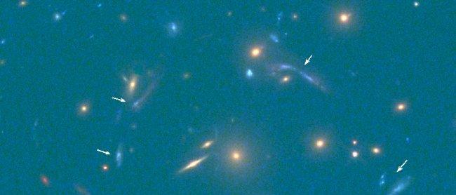 Imagen en el visible obtenida por el telescopio espacial Hubble. Las múltiples imágenes de la galaxia descubierta están señaladas por flechas blancas (abajo a la derecha aparece la escala de la imagen en segundos de arco).  