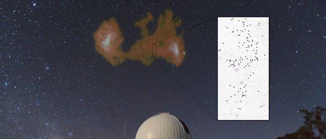 Las Nubes de Magallanes sobre el Telescopio Anglo-Australiano (AAT, Observatorio de Siding Spring, Australia). Superpuesto en falso color se muestra la distribución de gas atómico en ambas galaxias enanas y el Puente de Magallanes conectando las dos. El r