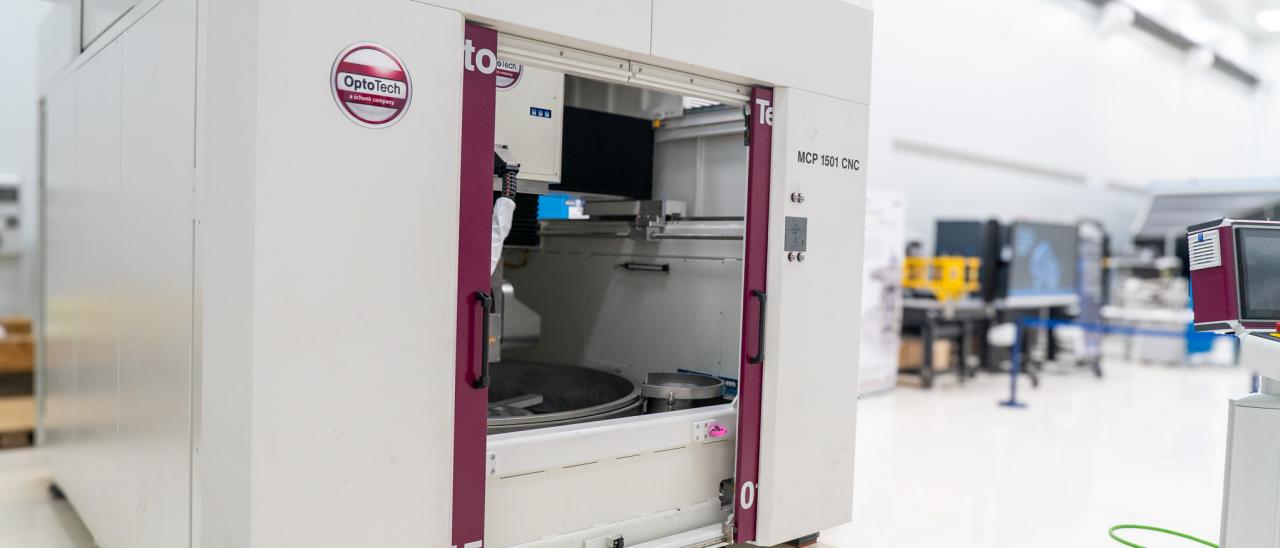 A large white machine with two big doors (polishing machine for large surfaces) in a white room with high ceilings (IACTEC's south clean room).