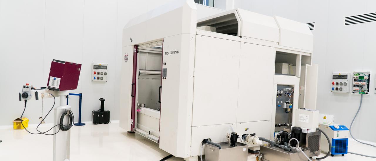 A large white machine with two big doors (polishing machine for large surfaces) in a white room with high ceilings (IACTEC's south clean room).