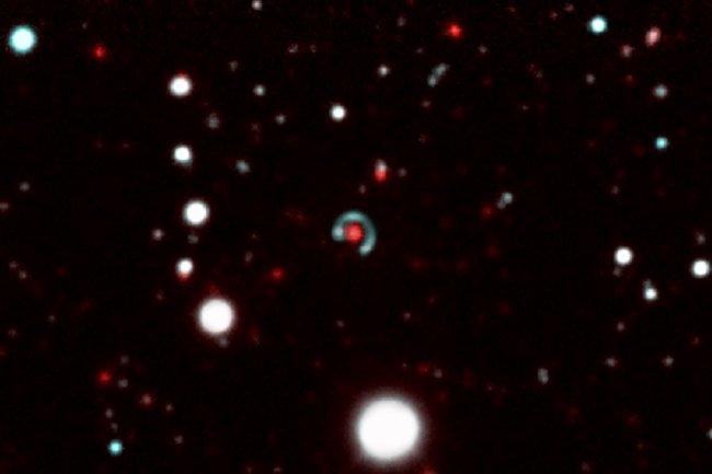 Image of the “Canarias Einstein ring”. In the centre of the picture, we can see how the source galaxy (the greenish-blue circle), which is further away “surrounds” the lens galaxy (red dot) almost completely. This phenomenon is produced because the strong