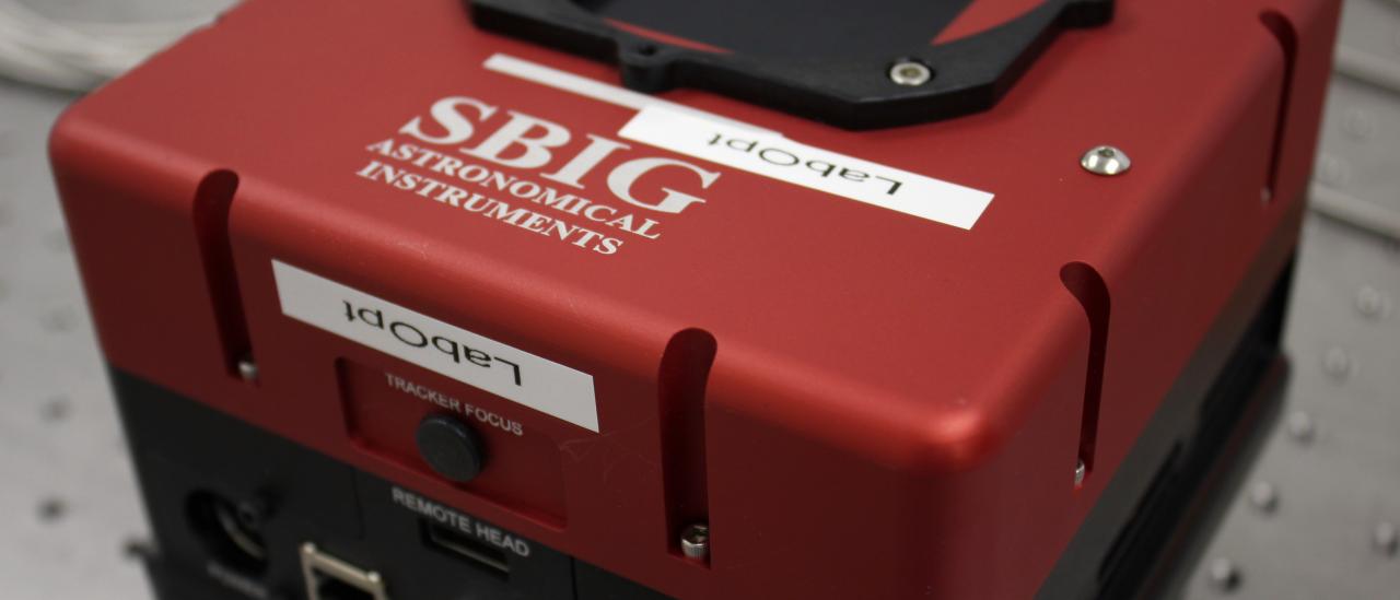 View of a SBIG camera on a table at the laboratory. Cubic shaped device with connectors.