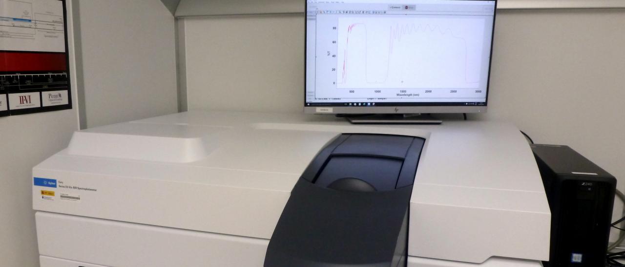 View of the spectrophotometer in the laboratory. Medium sized device placed on a table with a trap door to place the samples to be measured and a computer and monitor for its control