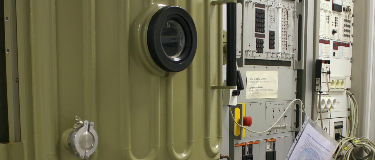 View of the evaporator and its associated electronics in the laboratory. Machine with a reinforced door and a porthole, and two large racks with electronic components, buttons and indicators for the control of the machine