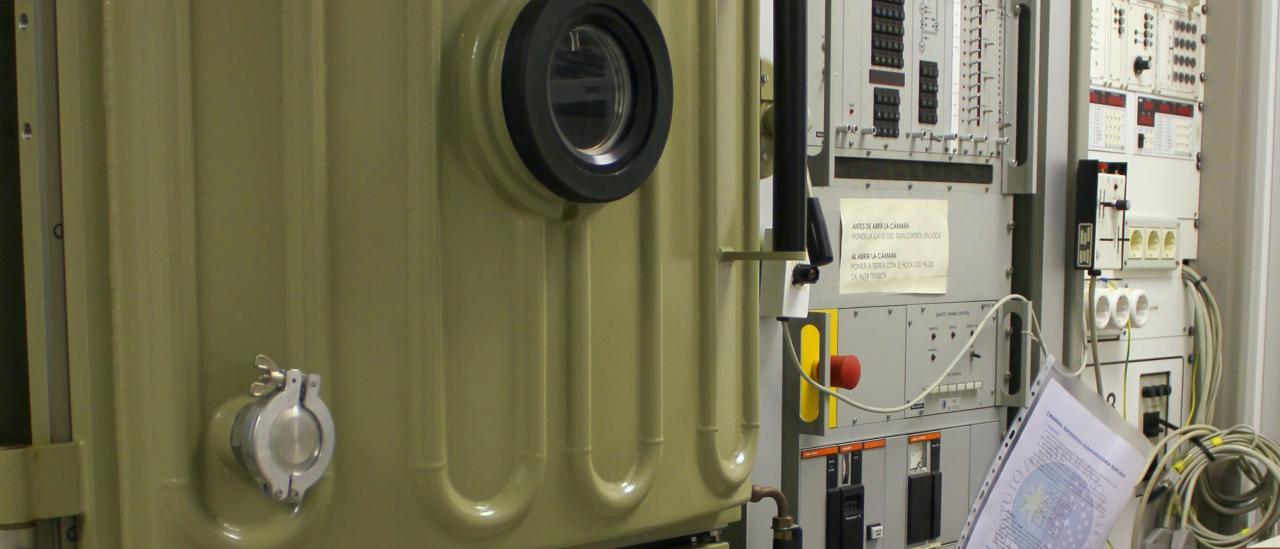 View of the evaporator machine and its associated electronics in the laboratory. View of the evaporator and its associated electronics in the laboratory. Machine with a reinforced door and a porthole, and two large racks with electronic components, buttons and indicators for the control of the machine