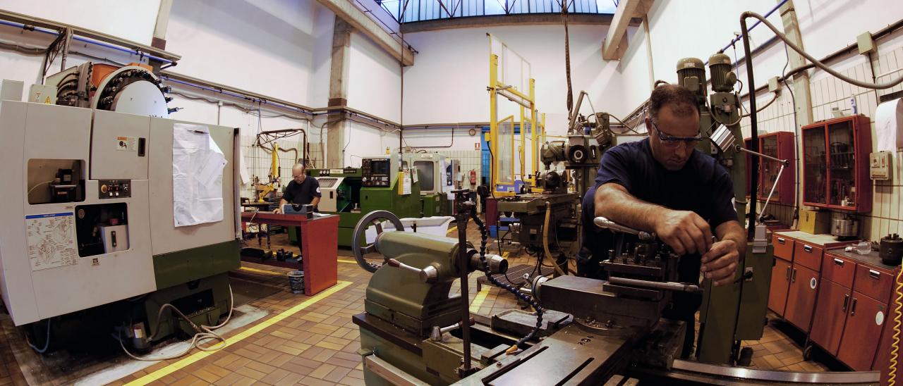 Partial view of the mechanics workshop with technicians working. Author A. L. Aldai. Large workshop with several manufacturing machines and a technician on the right adjusting a piece in one of them