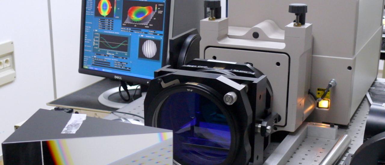 View of the interferometer on a optical table in the laboratory. Optoelectronic device with in front of a large prism and a lens with a computer monitor with graphics on the back