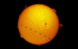 Representación artística del tránsito de Mercurio. La imagen muestra la dirección, de izquierda a derecha, que seguirá el planeta (representado a escala por el circulo negro) durante las siete horas y media que tarda en recorrer el disco solar. Las horas indicadas son en Tiempo Universal; se debe sumar una hora para Canarias y dos para el resto de España. Imagen del Sol en Halfa. Crédito: Daniel López/IAC.