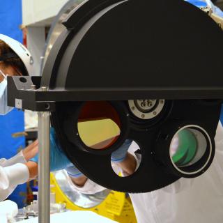 Image of an engineer working on the final assembly of the grisms wheel of the EMIR instrument in the laboratory. Large black metal wheel with holes for optical components