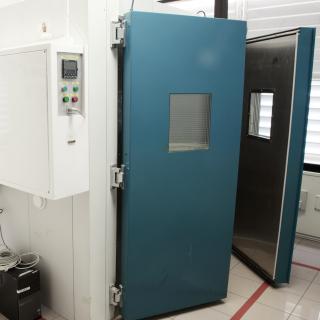 View of the environmental test chamber, a square enclosure with two thick half-open doors and a control panel with buttons, inside the laboratory