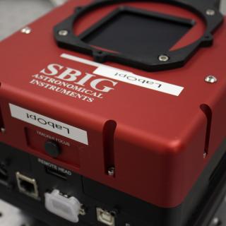 View of a SBIG camera on a table at the laboratory. Cubic shaped device with connectors.