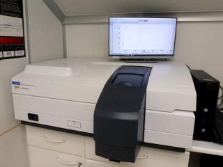 Vista del espectrofotómetro en el laboratorio. Aparato de tamaño medio colocado en una mesa con una trampilla para colocar las muestras a medir y un monitor y un ordenador para su control 