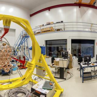 Panoramic view of one the areas of the Assembly, Integration and Verification room. Large laboratory with work benches and multiple electronic devices and computers, with a large mechanical structure in assembly phase