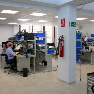 General view of the Electronics Workshop with several workbenches, cabinets and boxes to store components and electronic parts, and a technician working in one of the workbenches