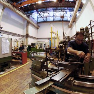 Vista de una parte del taller de mecánica con técnicos trabajando. Autor A. L. Aldai. Amplio taller con varias máquinas de fabricación mecánica y a la derecha un técnico ajustando una pieza en una de ellas