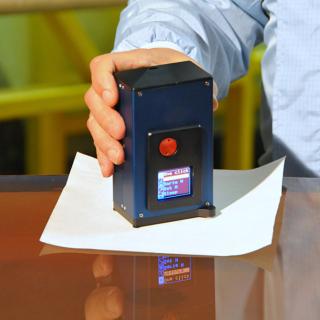 View of the CT7 reflectometer on a mirror. Author A1pixel View of the CT7 reflectometer on a mirror. Author A1pixel. Small device with a screen held by a technician's hand on the surface of a mirror