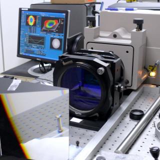 Vista del interferómetro en una mesa del laboratorio Vista del interferómetro en una mesa del laboratorio. Dipositivo optoelectrónico con una gran prisma y una lente delante y una pantalla de ordenador con gráficos detrás